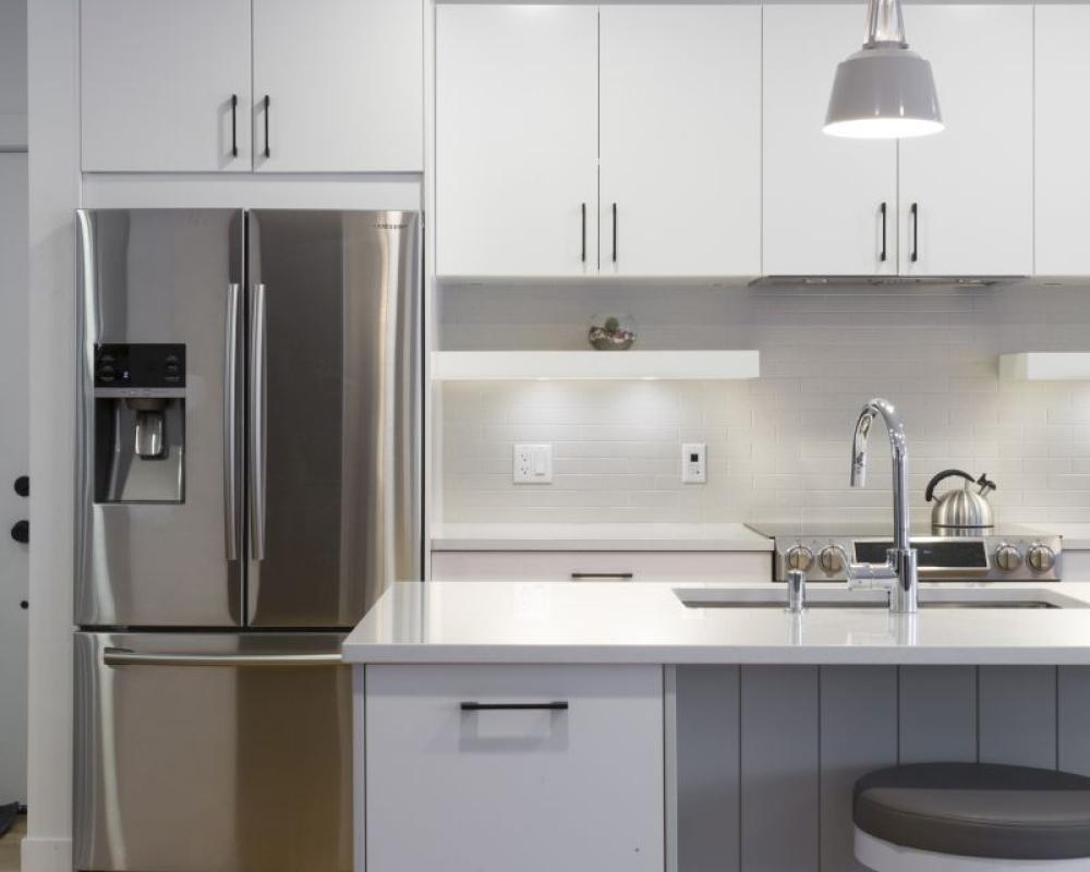 Bright kitchen with stainless steel oven, dishwasher, and refrigerator set against sleek white cabinetry