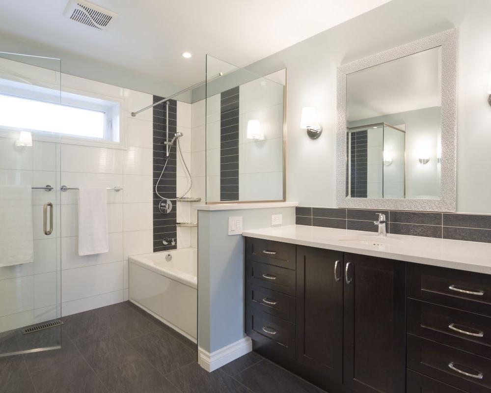 Contemporary bathroom with glass shower, bathtub, dark vanity cabinets, light countertop, large mirror, and modern lighting.